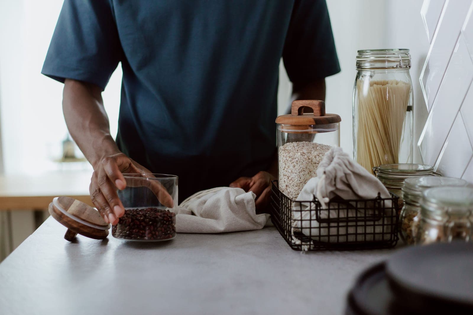 A glass brewing jar with a cloth cover on a bright kitchen counter beside loose tea and sugar