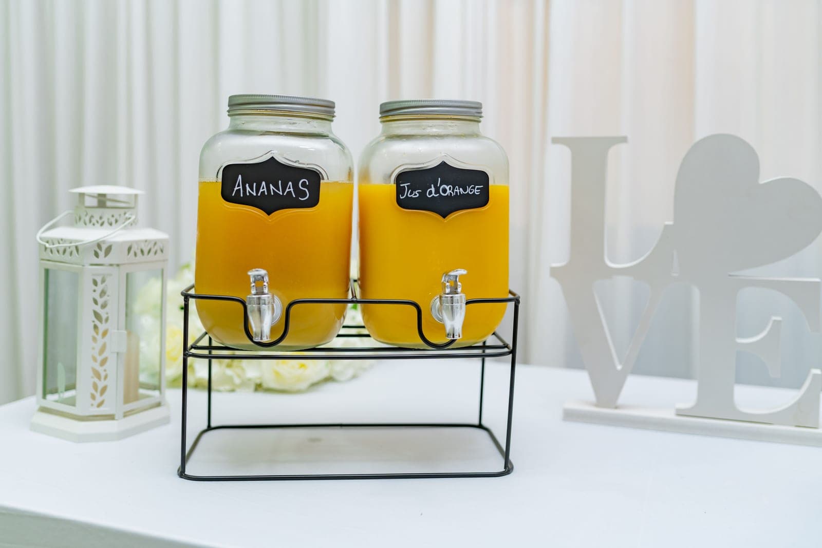 A large glass drink dispenser with a stainless steel tap standing on a pale kitchen counter